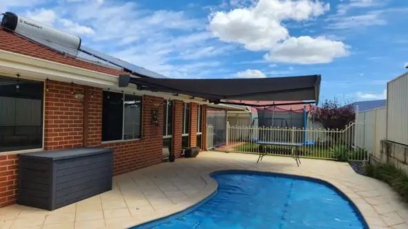 Folding arm awning shading a backyard swimming pool beside a brick home