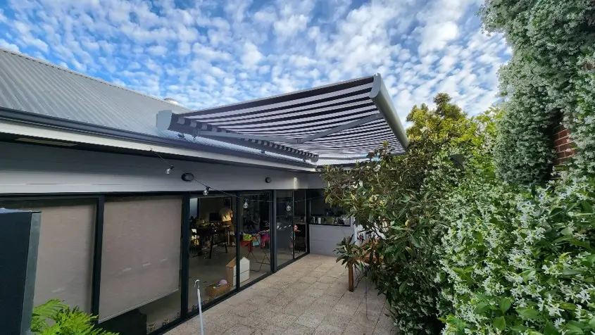 Striped folding arm awning extended over a modern alfresco area with glass sliding doors