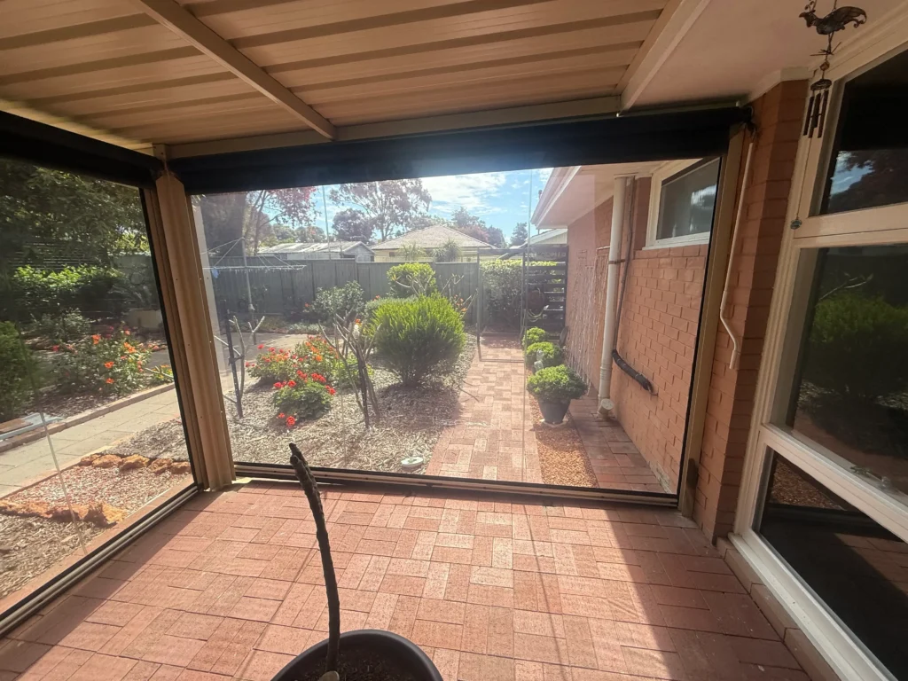 Inside a Rivervale patio with tinted PVC Ziptrak blinds and the garden visible beyond